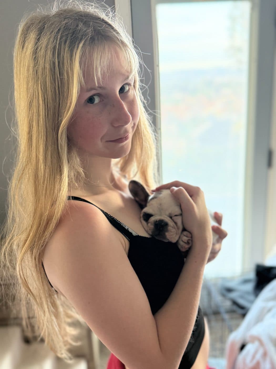 Brianna holding a sleeping French bulldog puppy by a bright window during a puppy visit in Westlake Village
